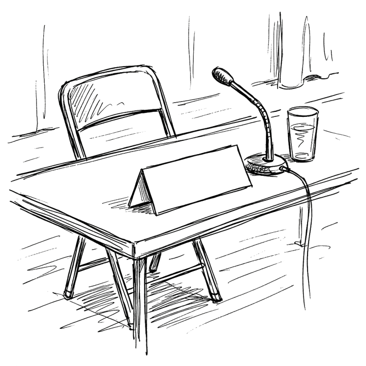 A blank tent-style place card on a panel-discussion desk, alongside a gooseneck microphone, a water glass, and a folding chair.